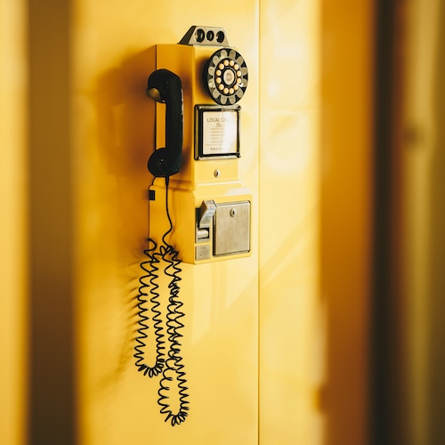 image of retro payphone mounted to a bright yellow wall